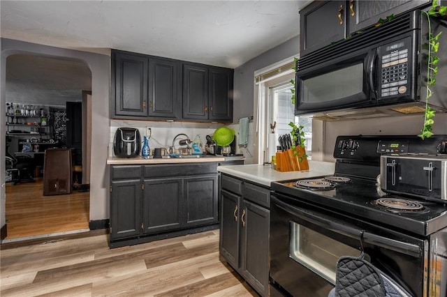 kitchen featuring light wood-type flooring, black appliances, a sink, backsplash, and light countertops