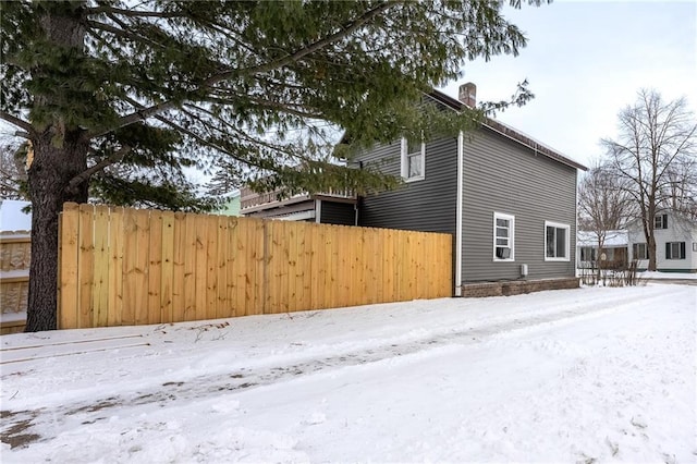 view of snow covered exterior with a chimney and fence