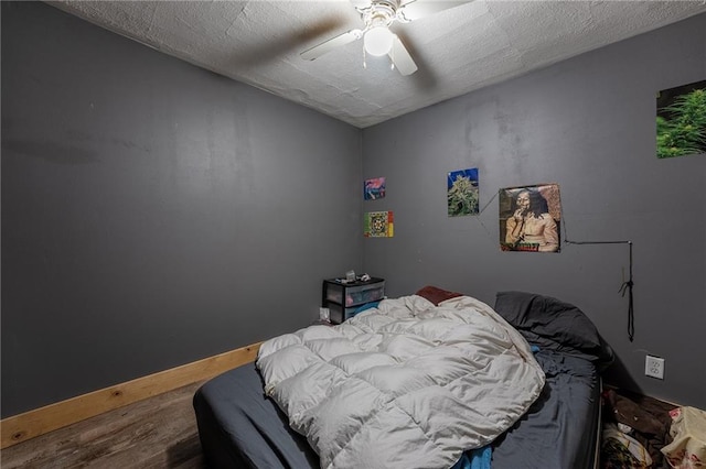 bedroom with a textured ceiling, a ceiling fan, baseboards, and wood finished floors