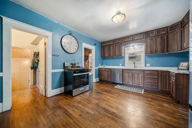 kitchen featuring stainless steel dishwasher, light countertops, dark wood-type flooring, and gas range oven