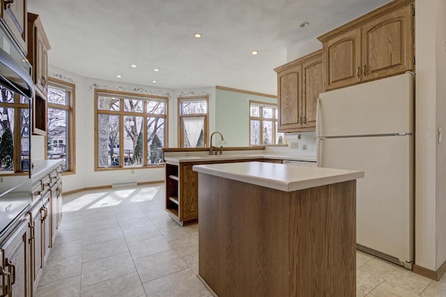 kitchen featuring a sink, a kitchen island, freestanding refrigerator, a peninsula, and light countertops