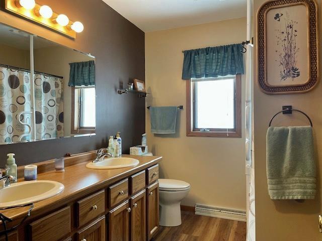 full bathroom with a sink, a baseboard radiator, toilet, and wood finished floors