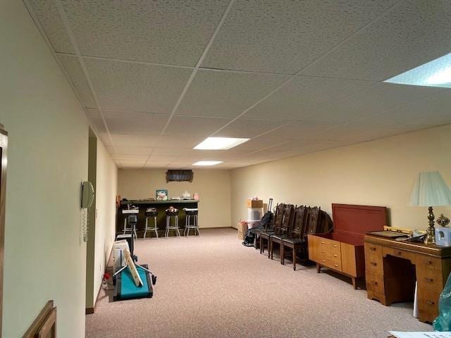 interior space with a paneled ceiling, carpet, and a dry bar