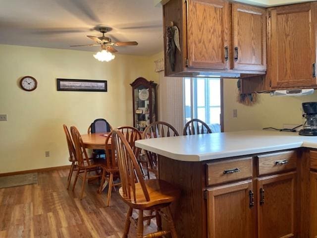 kitchen with a breakfast bar, light countertops, a peninsula, wood finished floors, and brown cabinetry