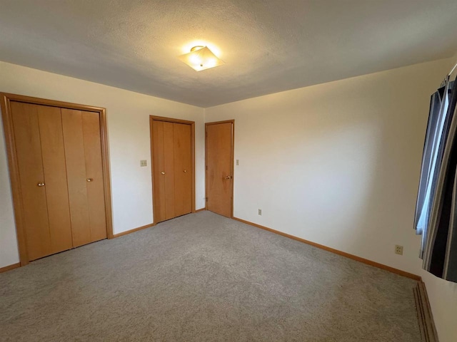 unfurnished bedroom featuring light carpet, baseboards, two closets, and a textured ceiling