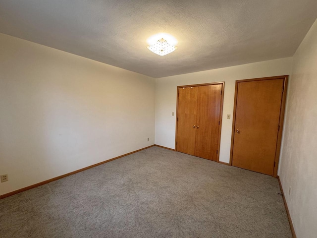 unfurnished bedroom with two closets, baseboards, carpet, and a textured ceiling