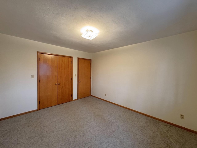 unfurnished bedroom featuring a textured ceiling, light colored carpet, multiple closets, and baseboards