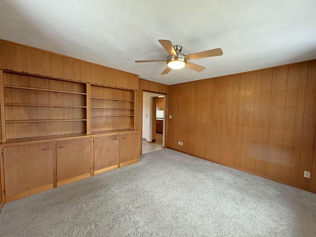 unfurnished bedroom featuring a ceiling fan, light colored carpet, and wood walls