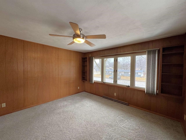 spare room with a ceiling fan, wooden walls, light colored carpet, and a baseboard radiator