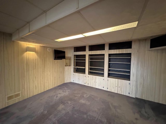 finished below grade area featuring carpet flooring, a paneled ceiling, visible vents, and wood walls