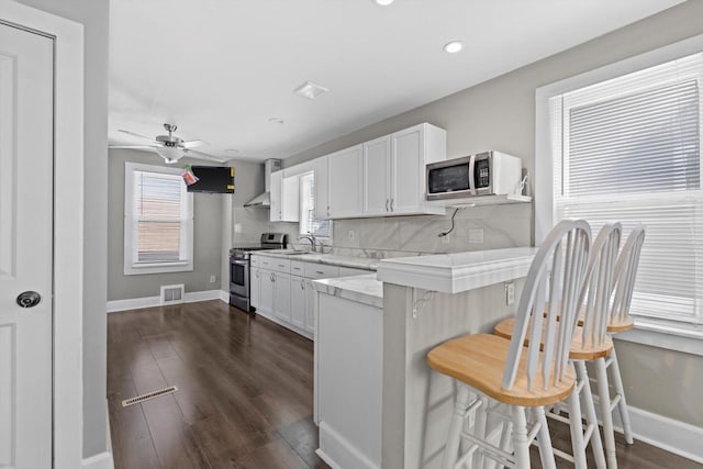 kitchen featuring visible vents, a sink, a kitchen breakfast bar, appliances with stainless steel finishes, and wall chimney range hood