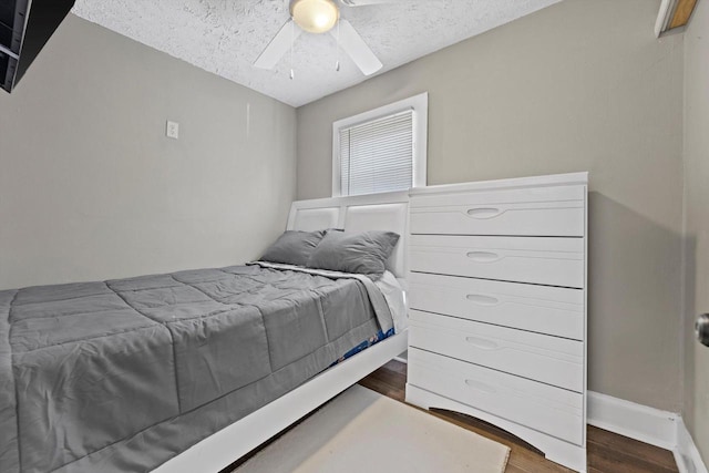 bedroom with ceiling fan, wood finished floors, baseboards, and a textured ceiling