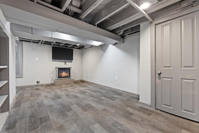 finished basement featuring baseboards, wood finished floors, and a glass covered fireplace