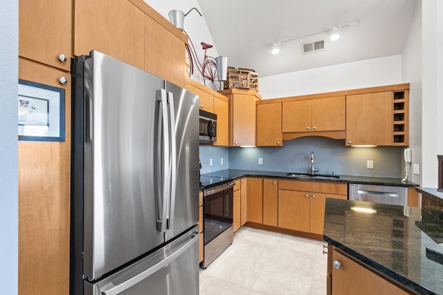 kitchen featuring dark stone countertops, visible vents, a sink, stainless steel appliances, and rail lighting