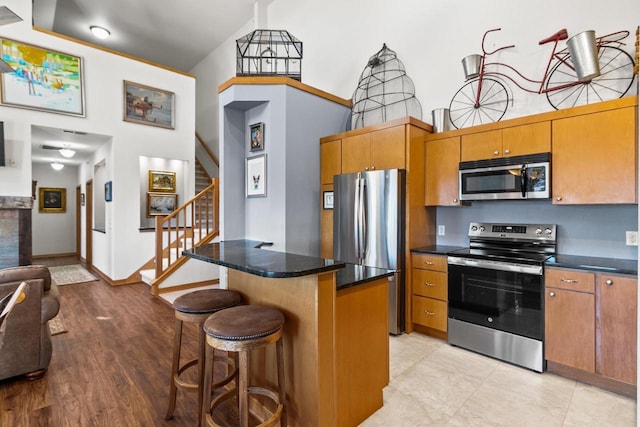 kitchen with brown cabinets, a breakfast bar, a center island, a high ceiling, and appliances with stainless steel finishes