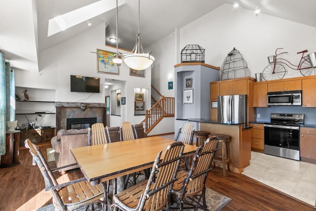 dining space with stairway, high vaulted ceiling, wood finished floors, and a tiled fireplace