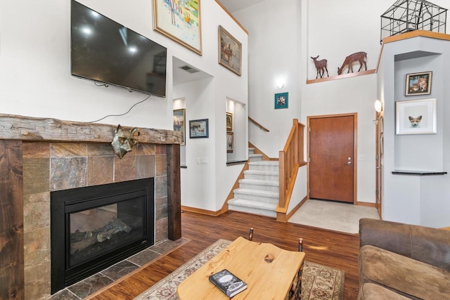 living room featuring wood finished floors, baseboards, a fireplace, stairs, and a towering ceiling