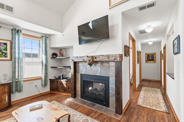 living area featuring a fireplace, wood finished floors, visible vents, and baseboards