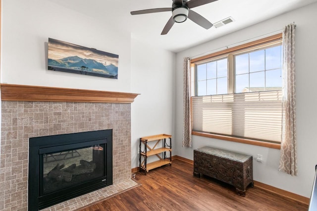 interior space featuring visible vents, a fireplace with flush hearth, a ceiling fan, wood finished floors, and baseboards