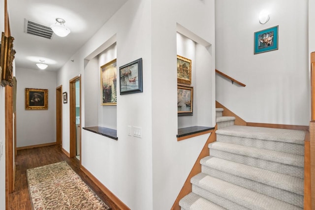 corridor with stairs, dark wood-type flooring, baseboards, and visible vents