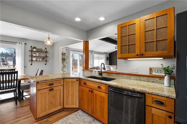 kitchen featuring light stone counters, a sink, glass insert cabinets, dishwasher, and light wood-type flooring