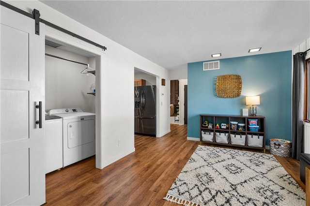 washroom featuring visible vents, washer and dryer, wood finished floors, a barn door, and baseboards