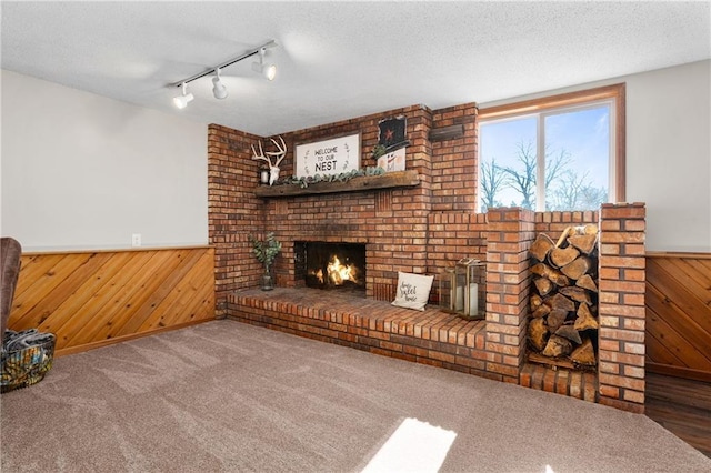 unfurnished living room with a wainscoted wall, a textured ceiling, a brick fireplace, and wood walls