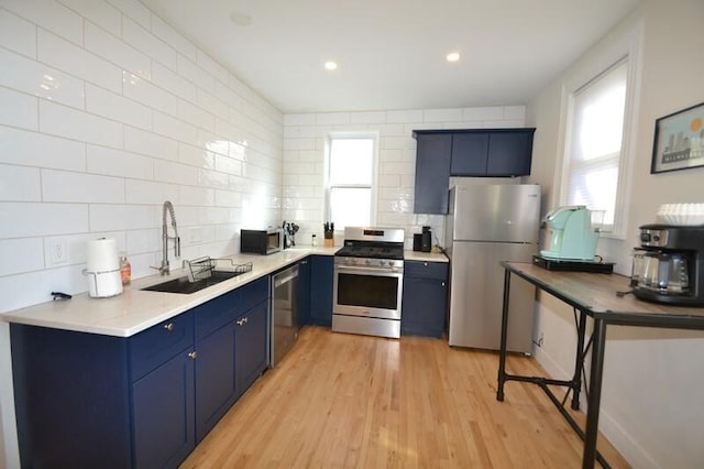 kitchen featuring blue cabinetry, light wood-type flooring, decorative backsplash, appliances with stainless steel finishes, and a sink