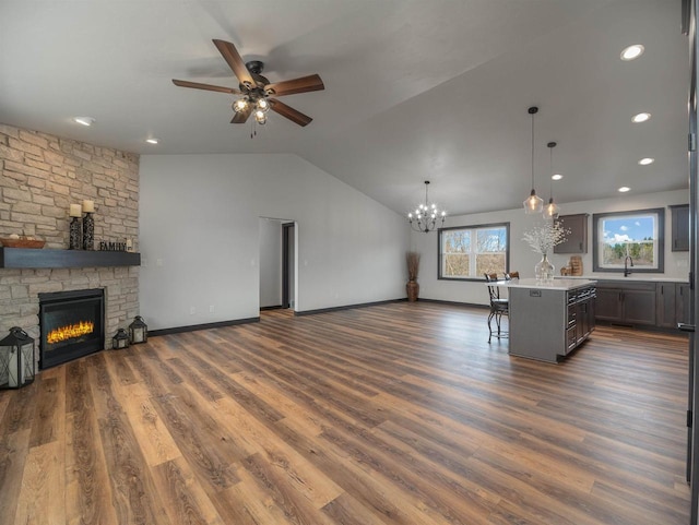 living area featuring a stone fireplace, dark wood finished floors, a ceiling fan, and vaulted ceiling