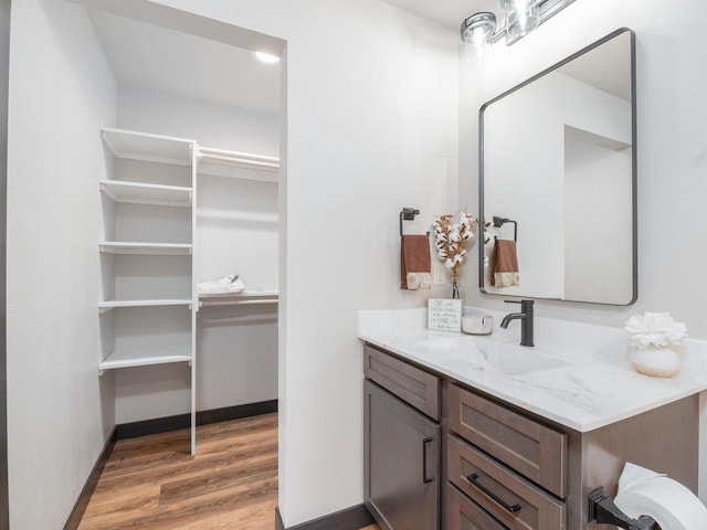 bathroom featuring vanity, a walk in closet, baseboards, and wood finished floors