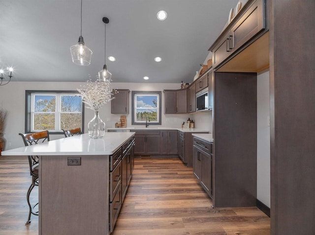 kitchen featuring a sink, decorative light fixtures, a kitchen breakfast bar, wood finished floors, and a center island