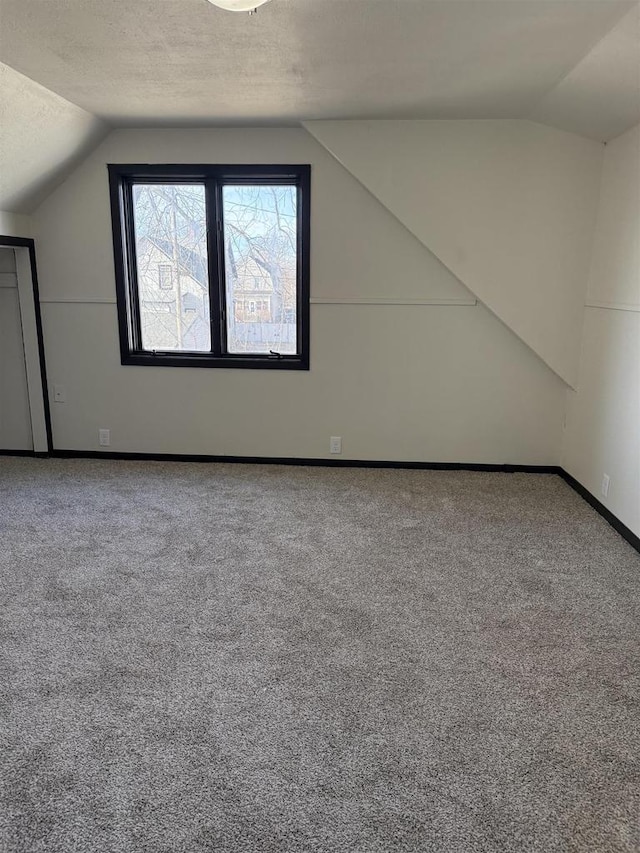 additional living space with baseboards, a textured ceiling, carpet flooring, and vaulted ceiling