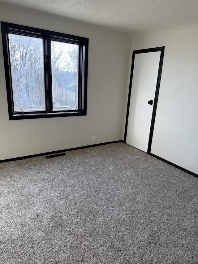 carpeted spare room featuring visible vents, baseboards, and a textured ceiling