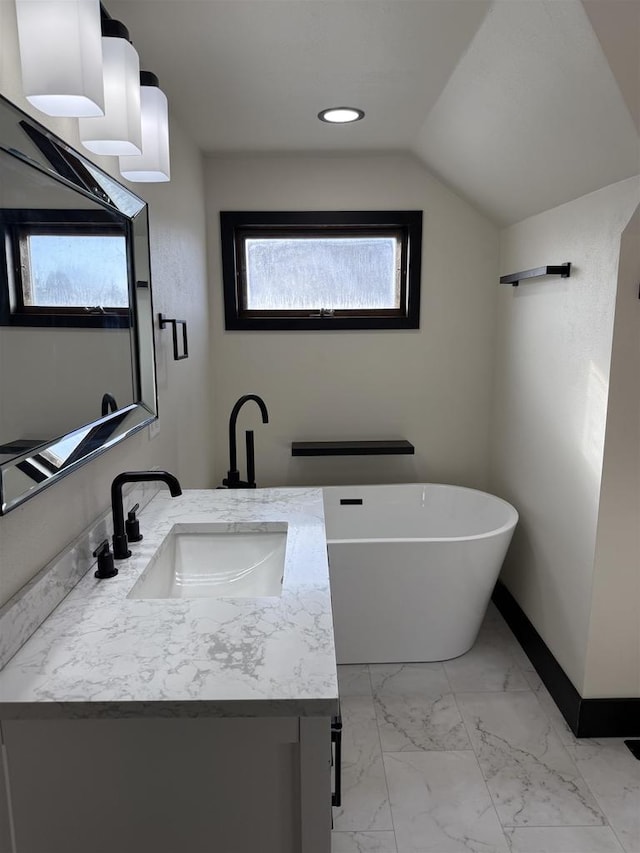 bathroom featuring marble finish floor, baseboards, a freestanding bath, vanity, and vaulted ceiling