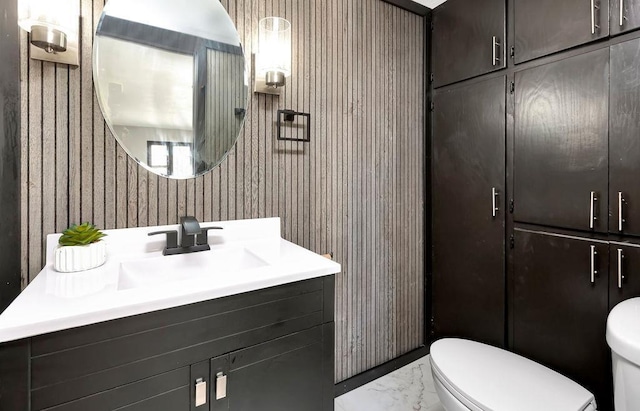 half bath with marble finish floor, toilet, and vanity