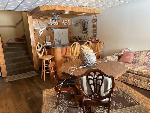 dining space featuring a bar, wood finished floors, stairway, and a paneled ceiling