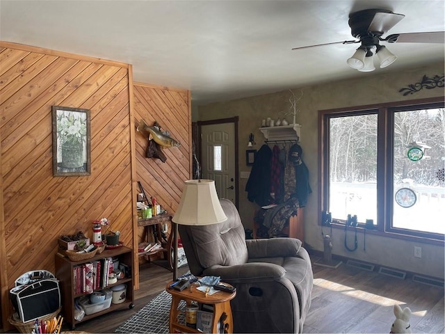 living area featuring ceiling fan, wooden walls, and wood finished floors