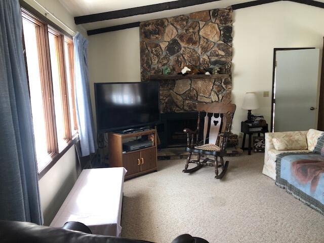 carpeted living area featuring a stone fireplace, beam ceiling, and plenty of natural light