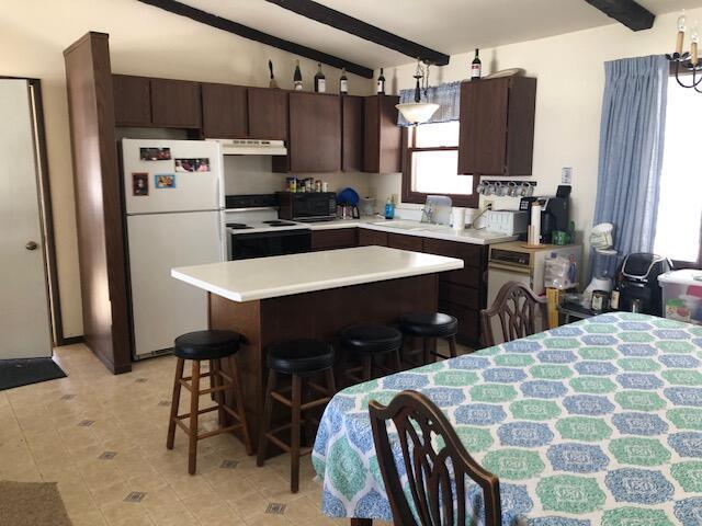 kitchen with under cabinet range hood, white appliances, a breakfast bar area, dark brown cabinets, and vaulted ceiling with beams