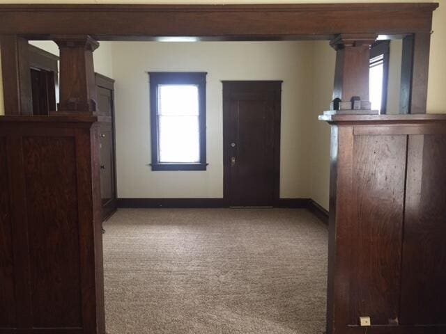 carpeted empty room with decorative columns and baseboards