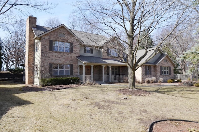 traditional-style house with brick siding, a front lawn, fence, a porch, and a chimney