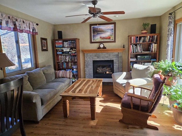 living area with a brick fireplace, ceiling fan, and wood finished floors