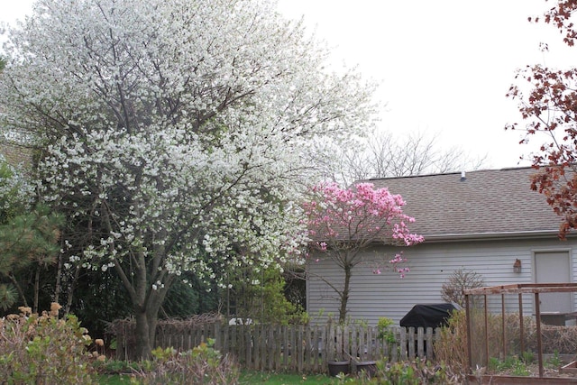 view of side of home featuring fence and a shingled roof