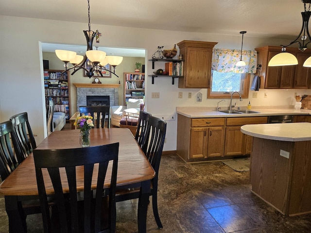 kitchen featuring a sink, brown cabinetry, a fireplace, light countertops, and hanging light fixtures