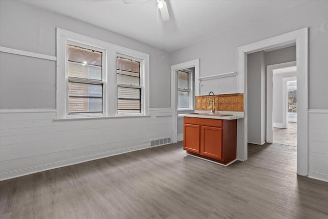 kitchen with wood finished floors, a wainscoted wall, visible vents, a sink, and light countertops