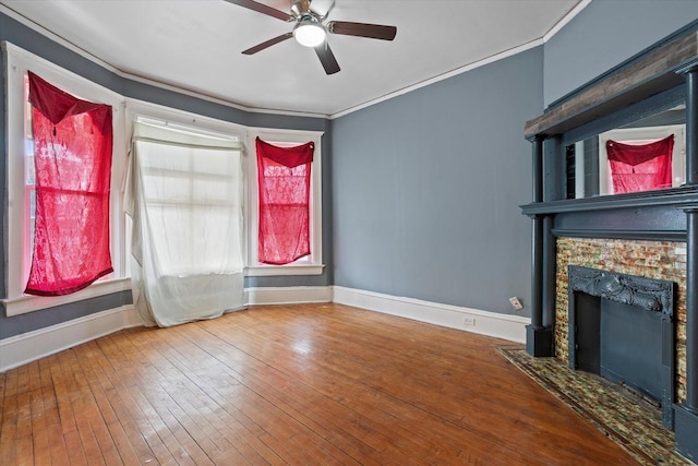 unfurnished living room featuring a stone fireplace, crown molding, baseboards, and hardwood / wood-style flooring