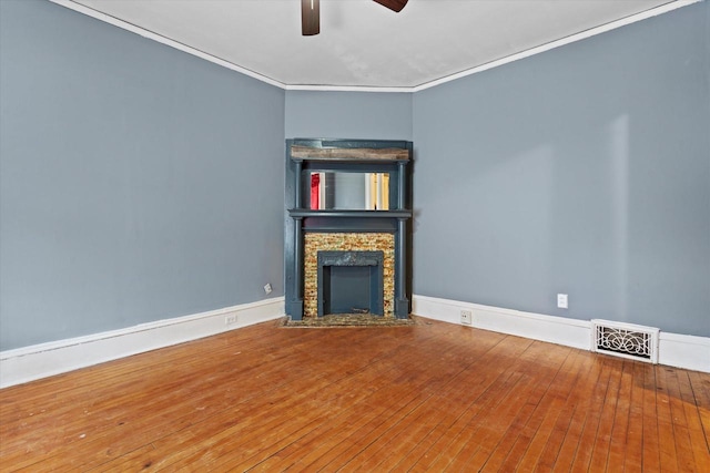 unfurnished living room with a stone fireplace, visible vents, wood-type flooring, and ornamental molding