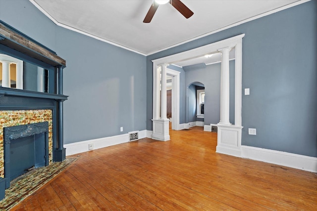 unfurnished living room with ornamental molding, hardwood / wood-style flooring, a premium fireplace, ceiling fan, and ornate columns