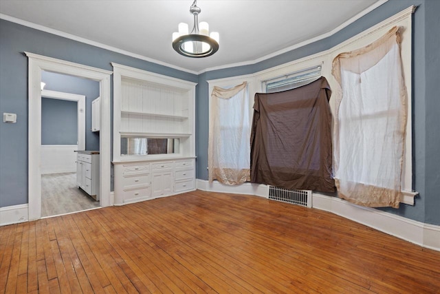 unfurnished bedroom with visible vents, a notable chandelier, wood-type flooring, crown molding, and baseboards