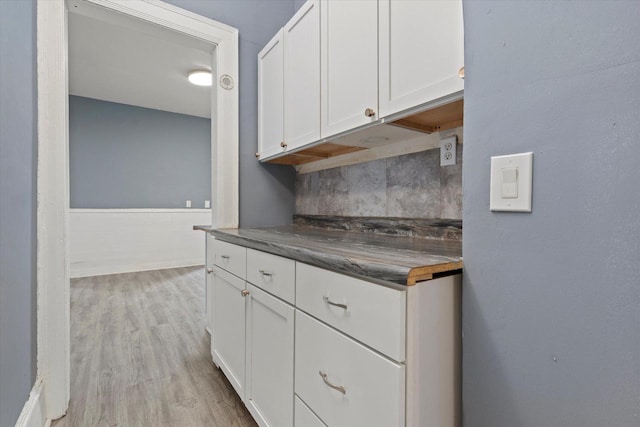 kitchen featuring tasteful backsplash, white cabinets, dark countertops, and light wood-type flooring